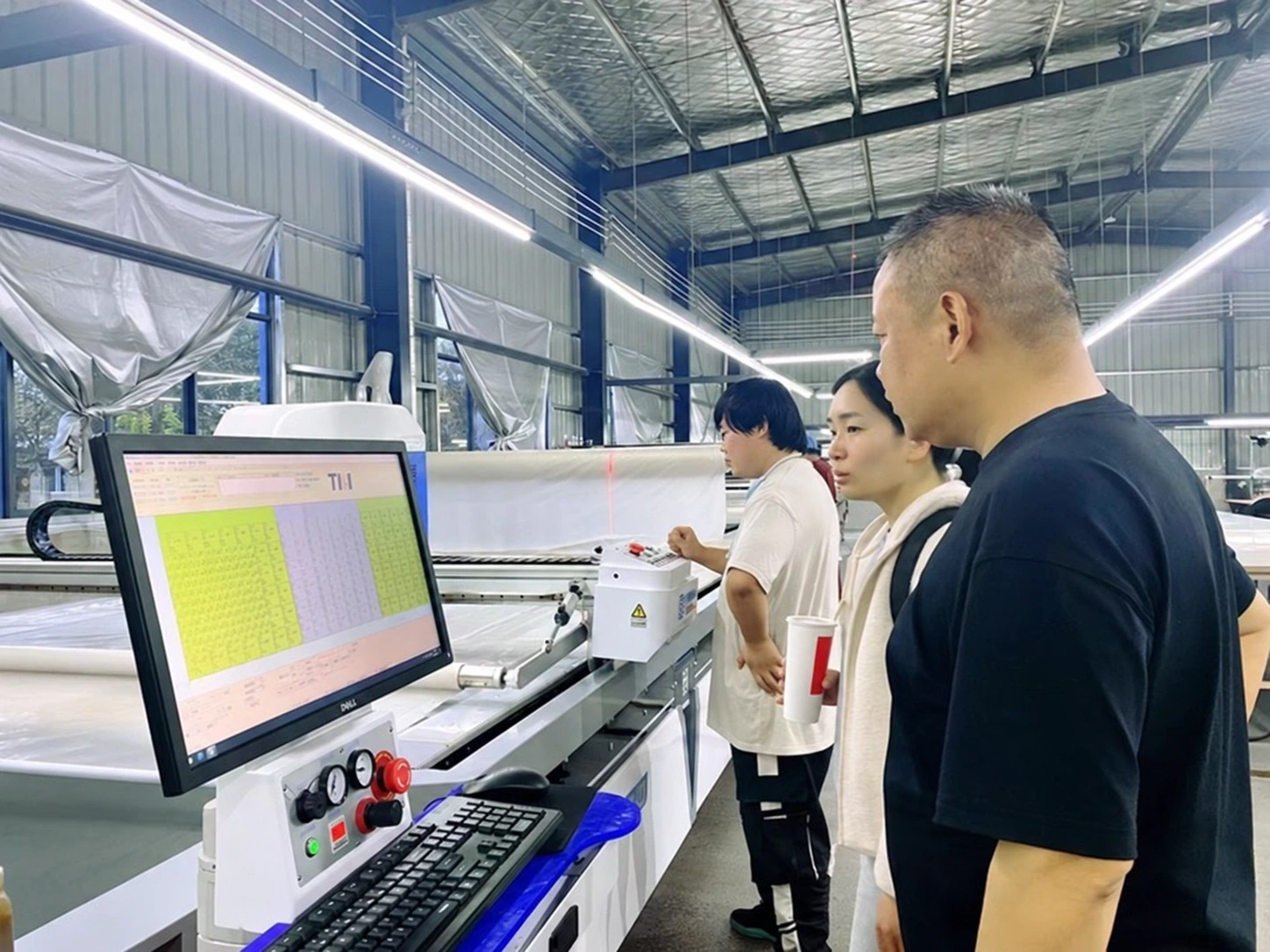 People reviewing a cutting-machine control screen in the workshop