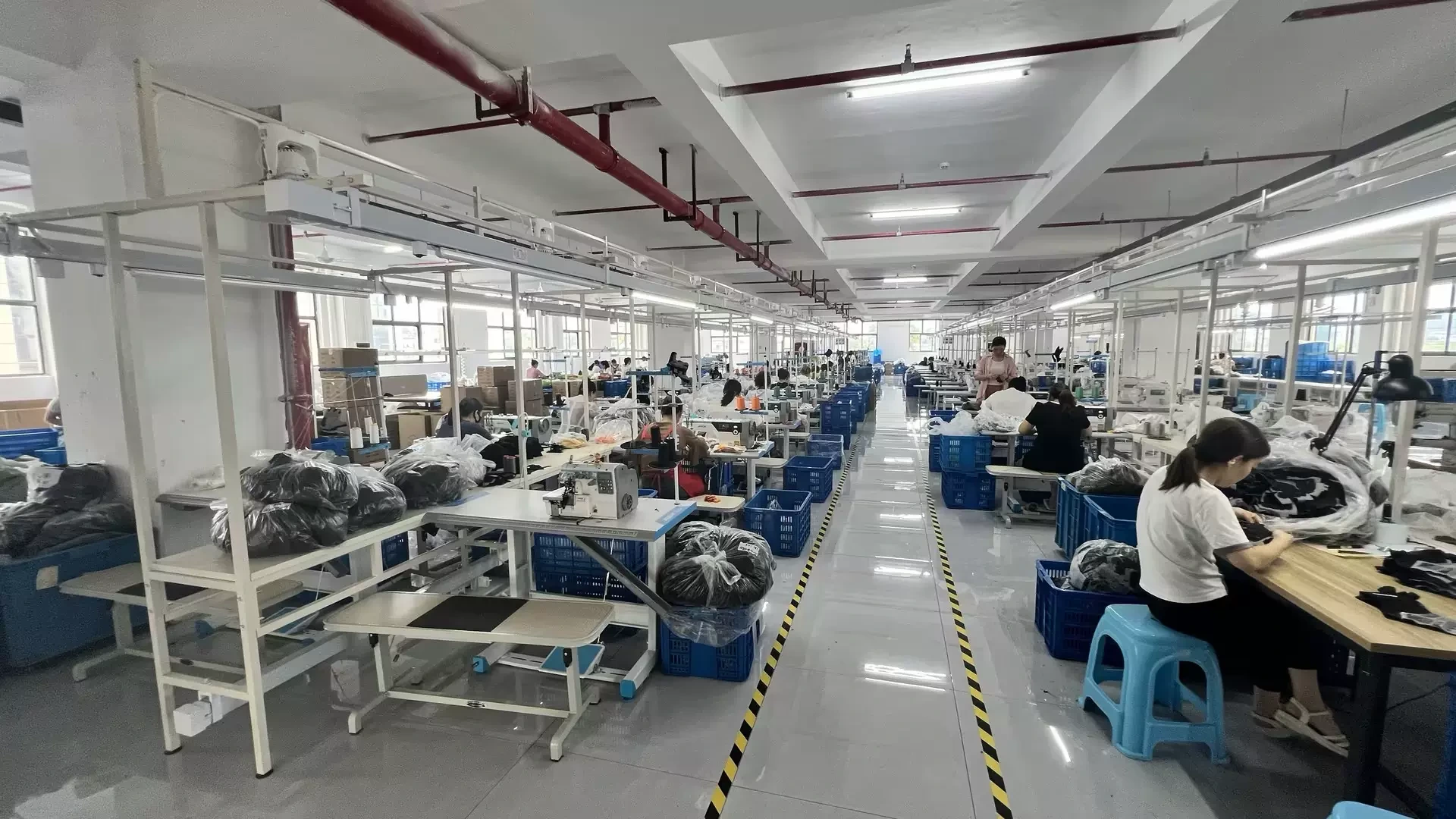 A sewing workshop with rows of workstations and blue storage bins