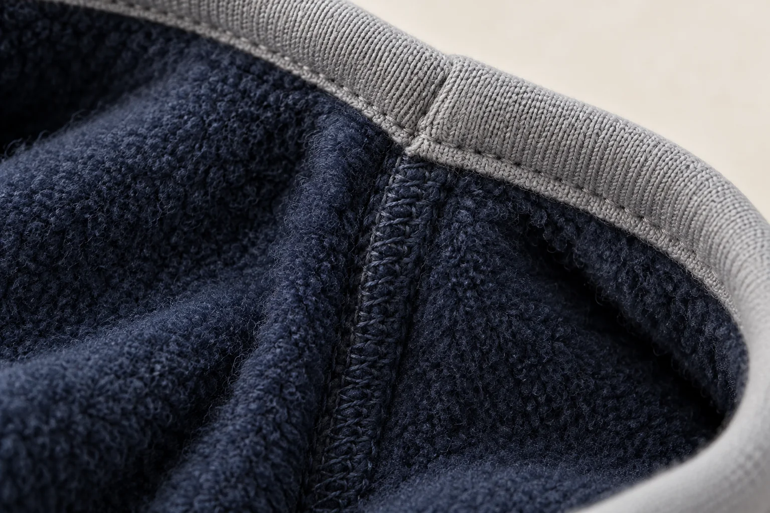 Navy fleece glove: inside view macro of light gray cuff binding where its overlap joins internal side seam.