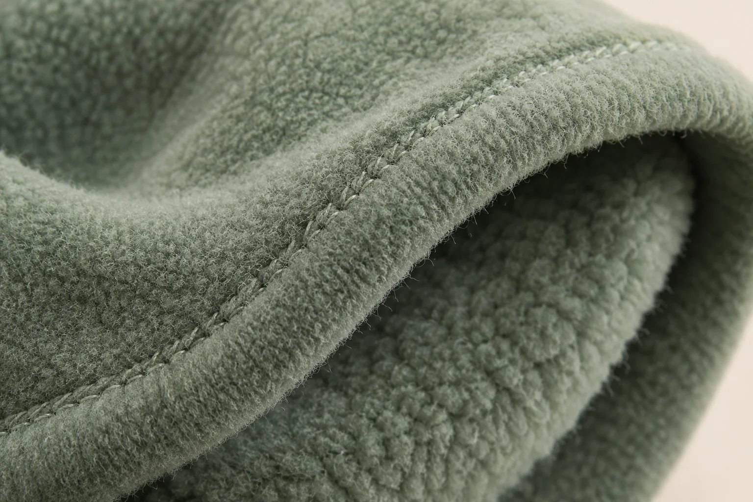 Sage fleece glove: macro same-material turned cuff hem with tiny matching stitch line, soft fleece interior visible alongside narrow rim.