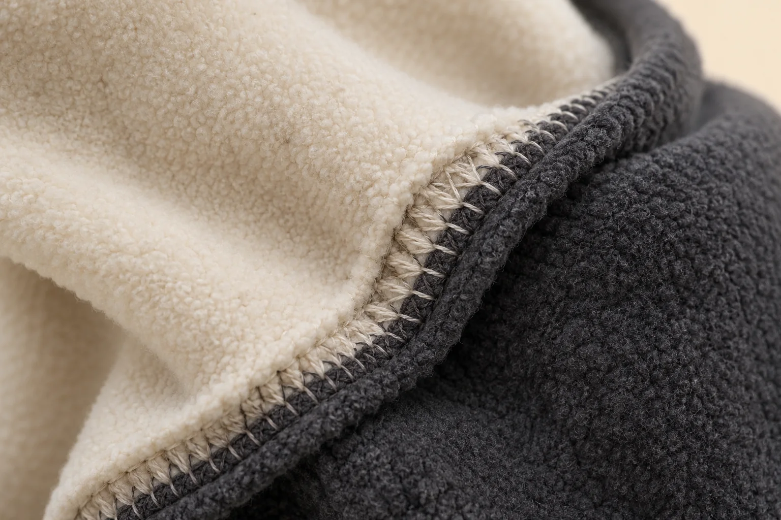 Cream hand / charcoal cuff fleece glove: inside macro of color-join seam.