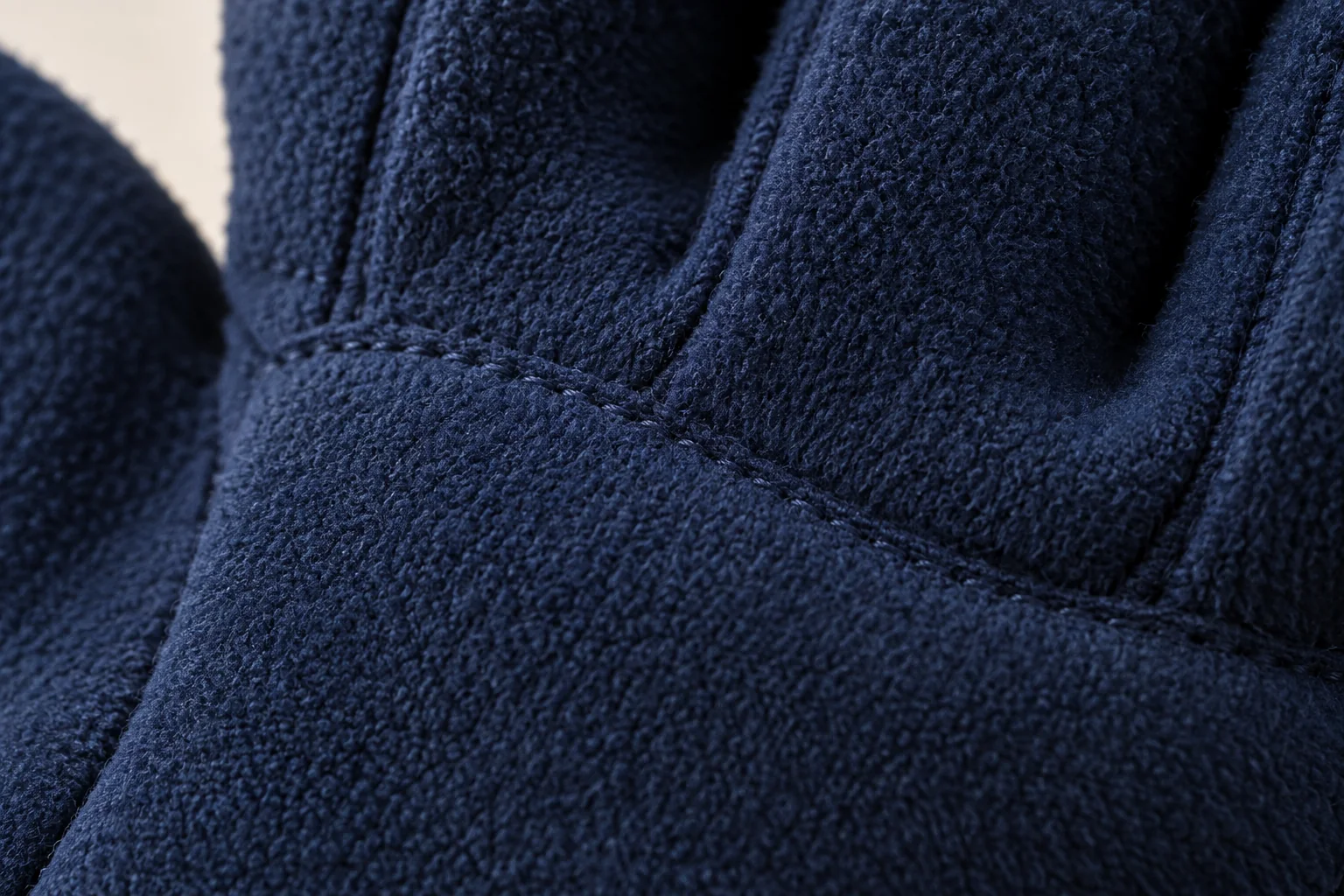 Navy fleece glove: tight macro of finger-base panel seam on the palm side.