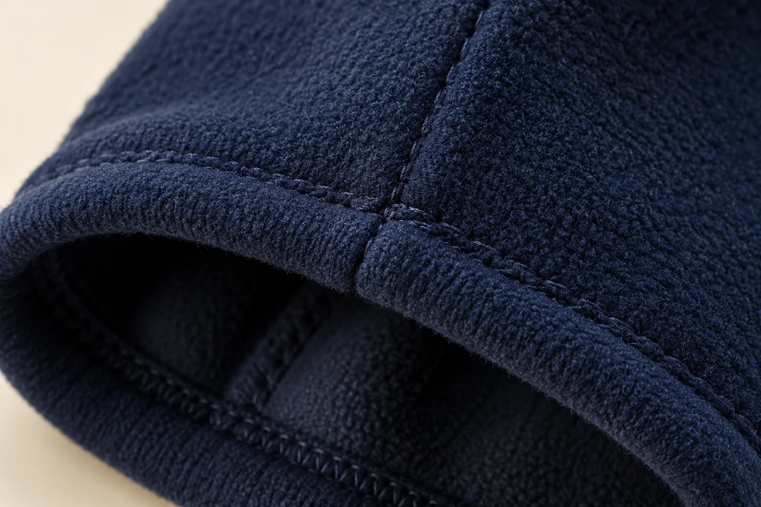 Navy fleece touchscreen glove: macro inside cuff hem at sewn side-seam intersection.