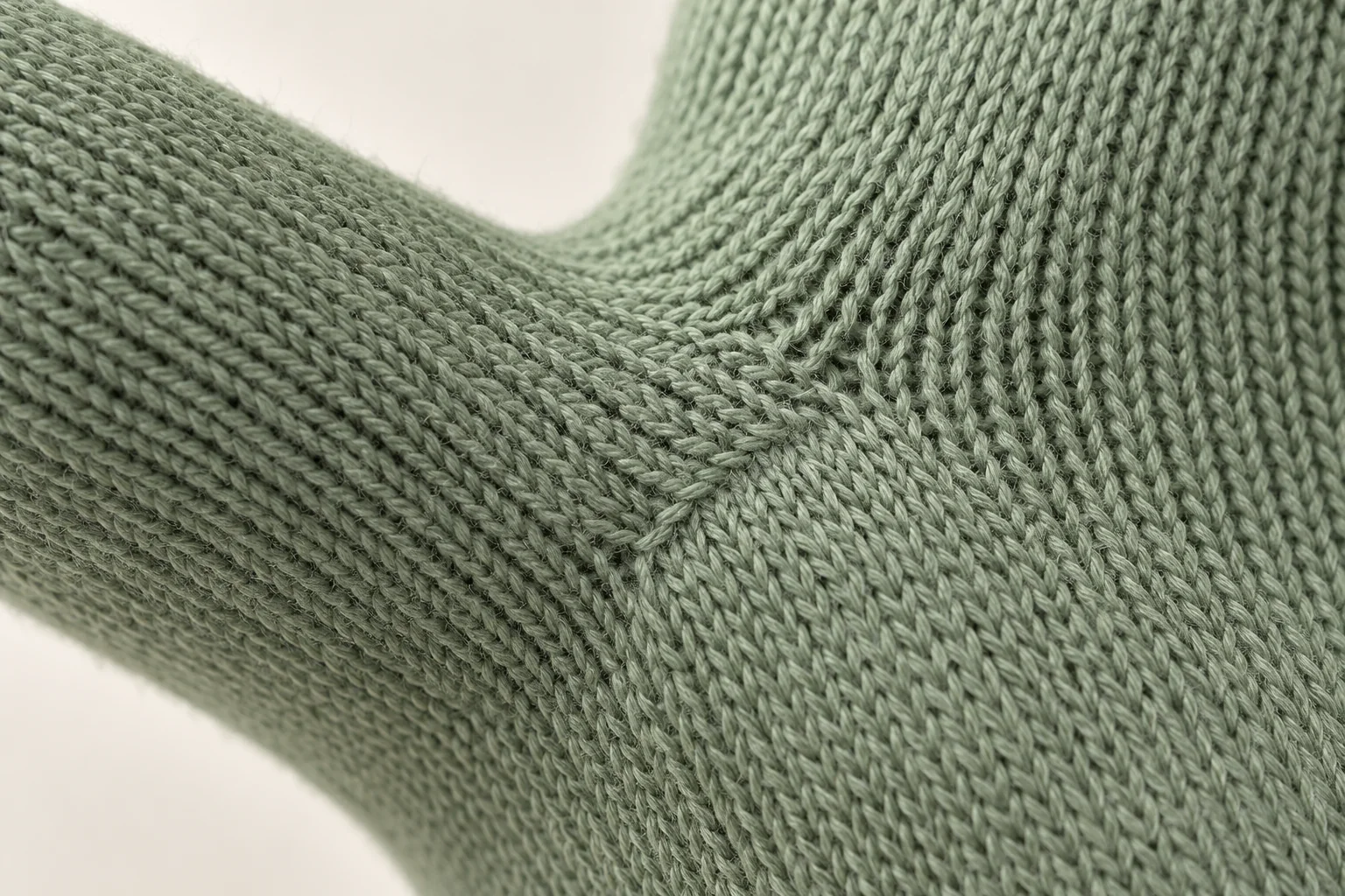 Sage-green knit glove: tight thumb-gusset to palm junction.