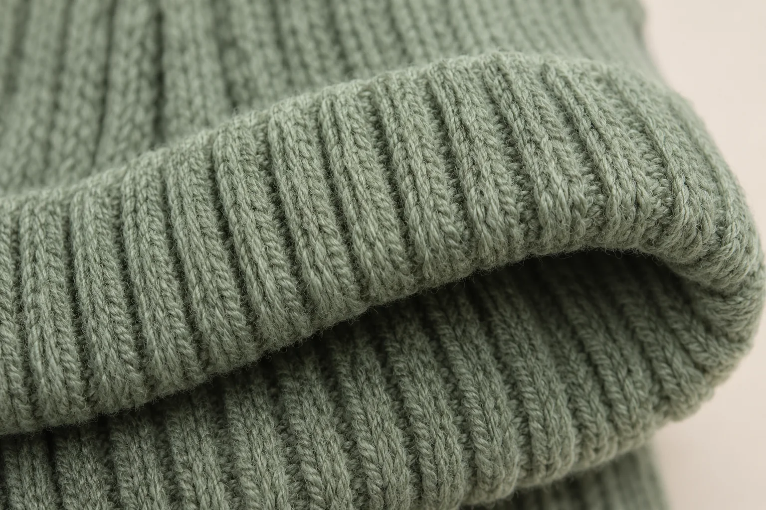 Sage-green glove: extreme close-up of folded-over rib cuff edge.