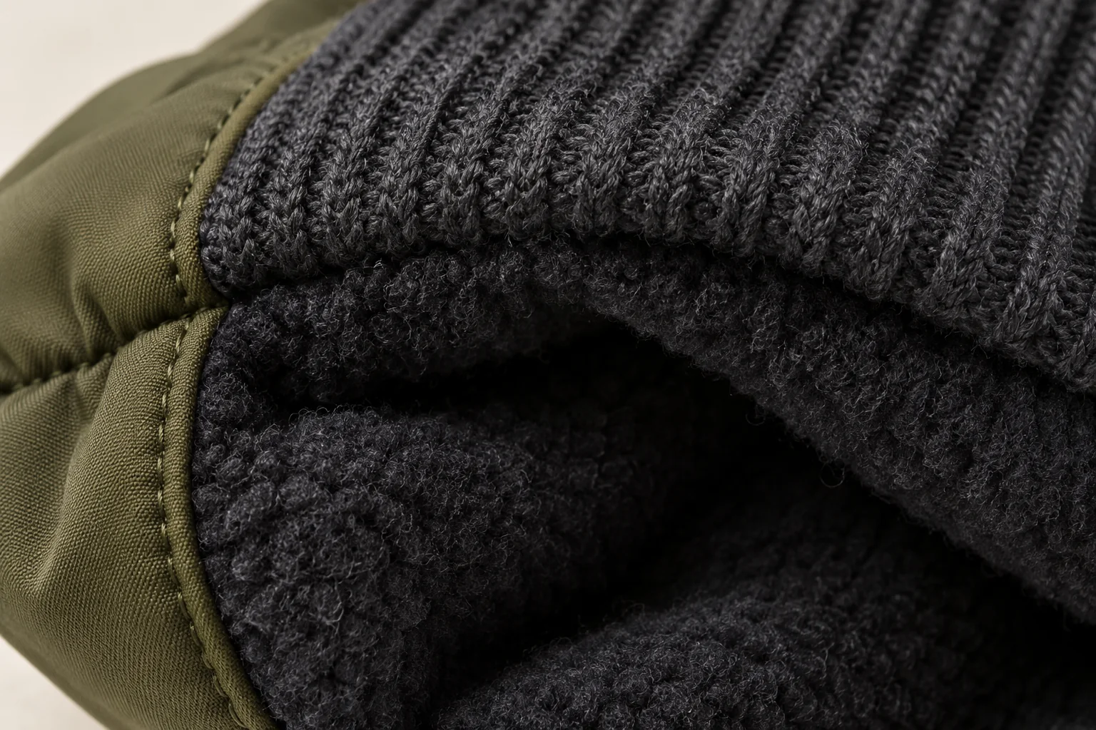 Olive shell / charcoal rib winter glove: macro inside wrist at dark fleece lining attachment beneath charcoal rib.