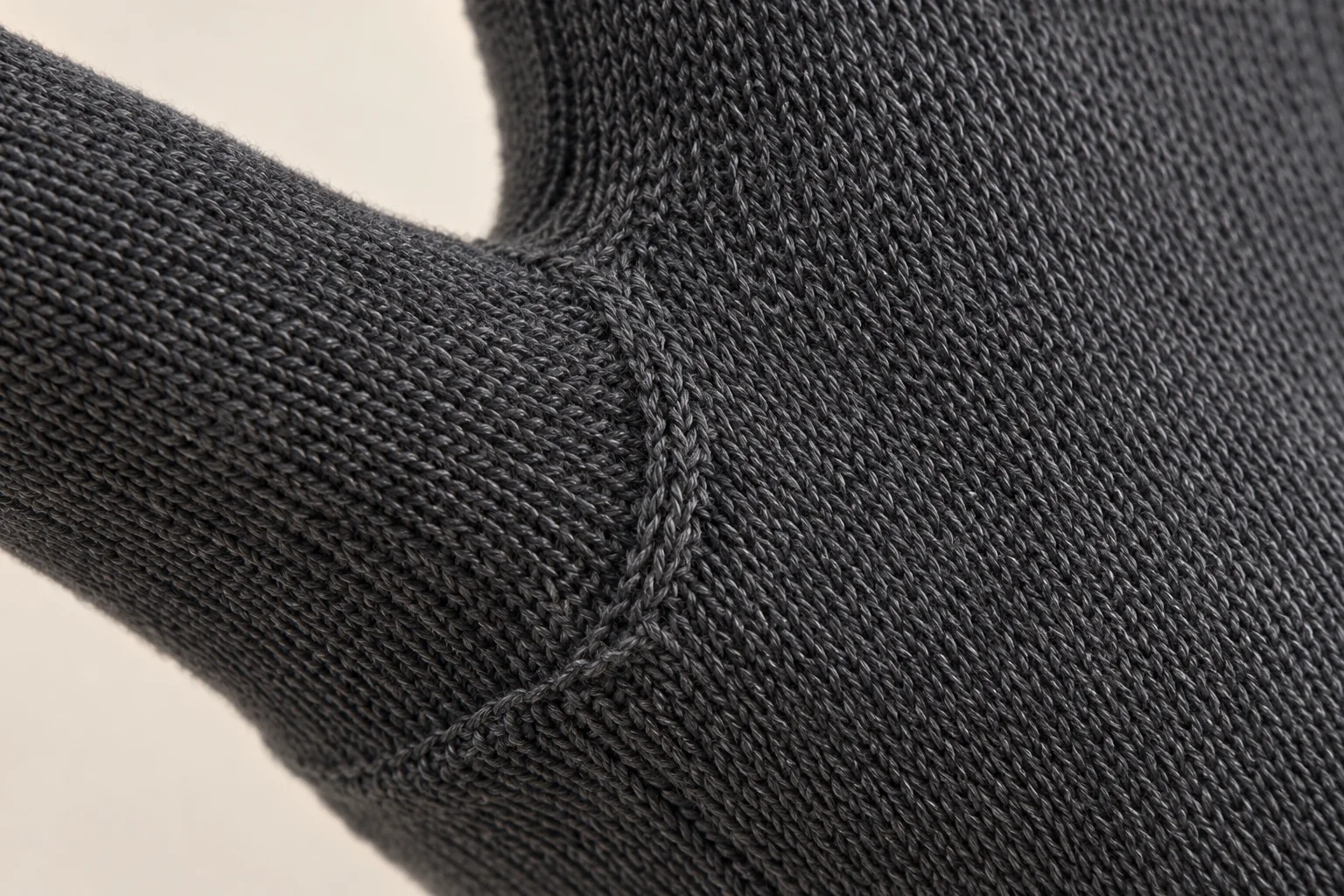 Charcoal knit glove: macro at palm-thumb gusset showing regular V loops and directional knit shaping.
