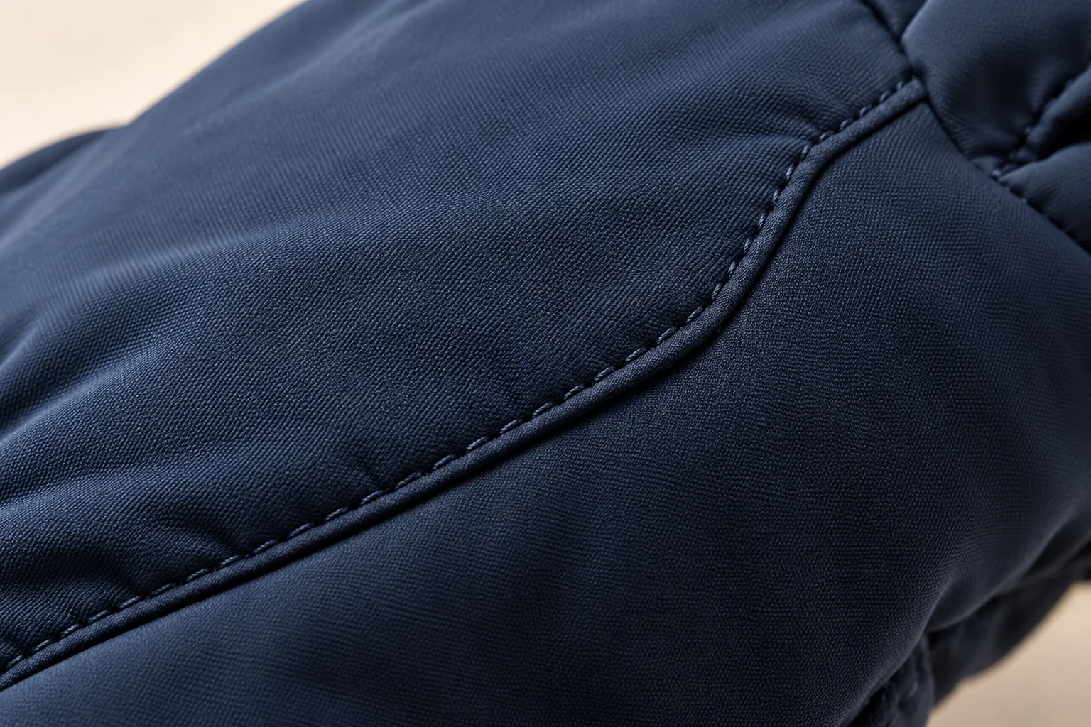 Navy woven-shell winter glove: macro curved diagonal hand-back seam through fine smooth navy shell.