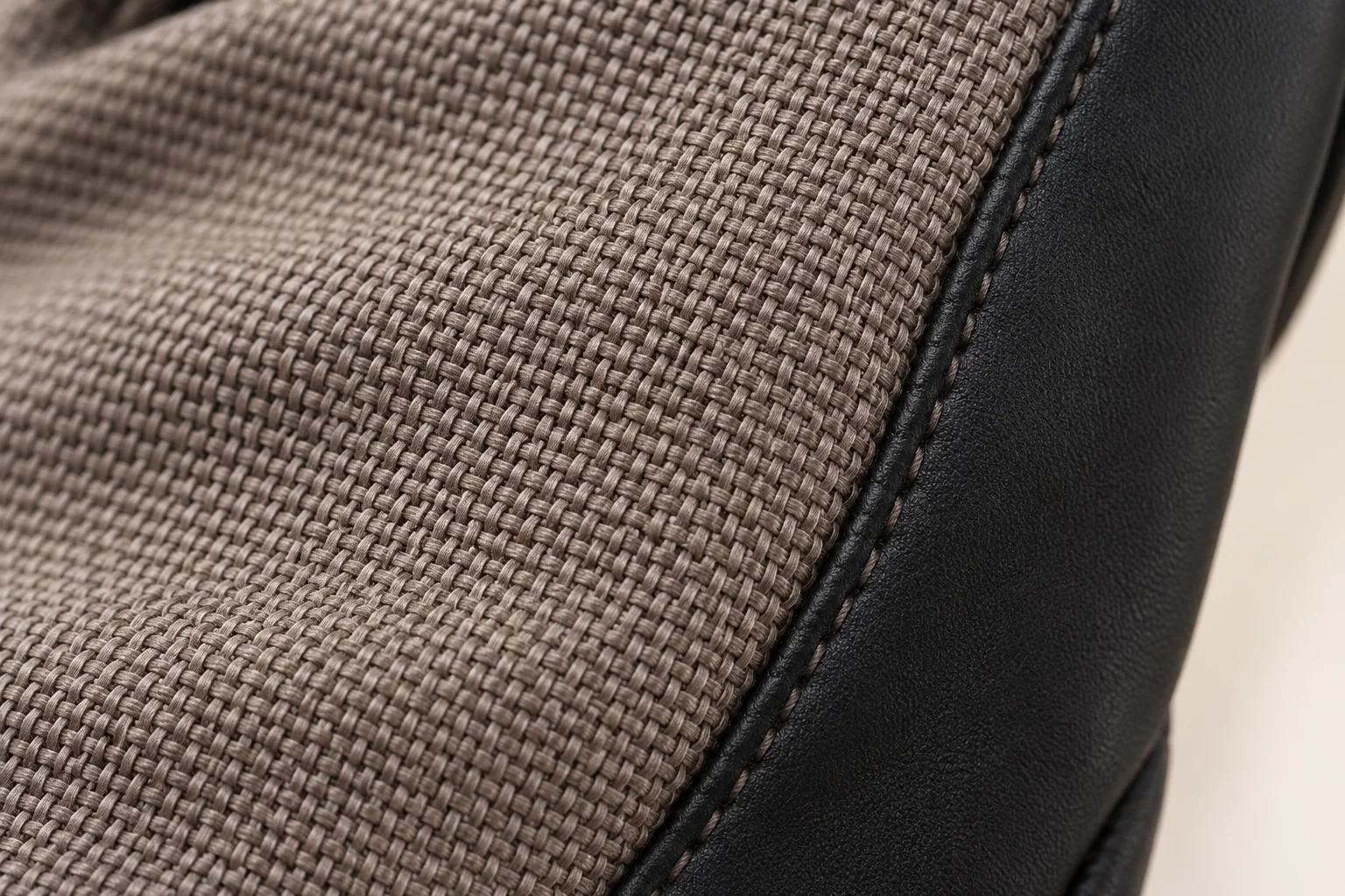 Mixed-panel touchscreen glove: macro taupe woven back joining a black smooth side strip along a curved seam.