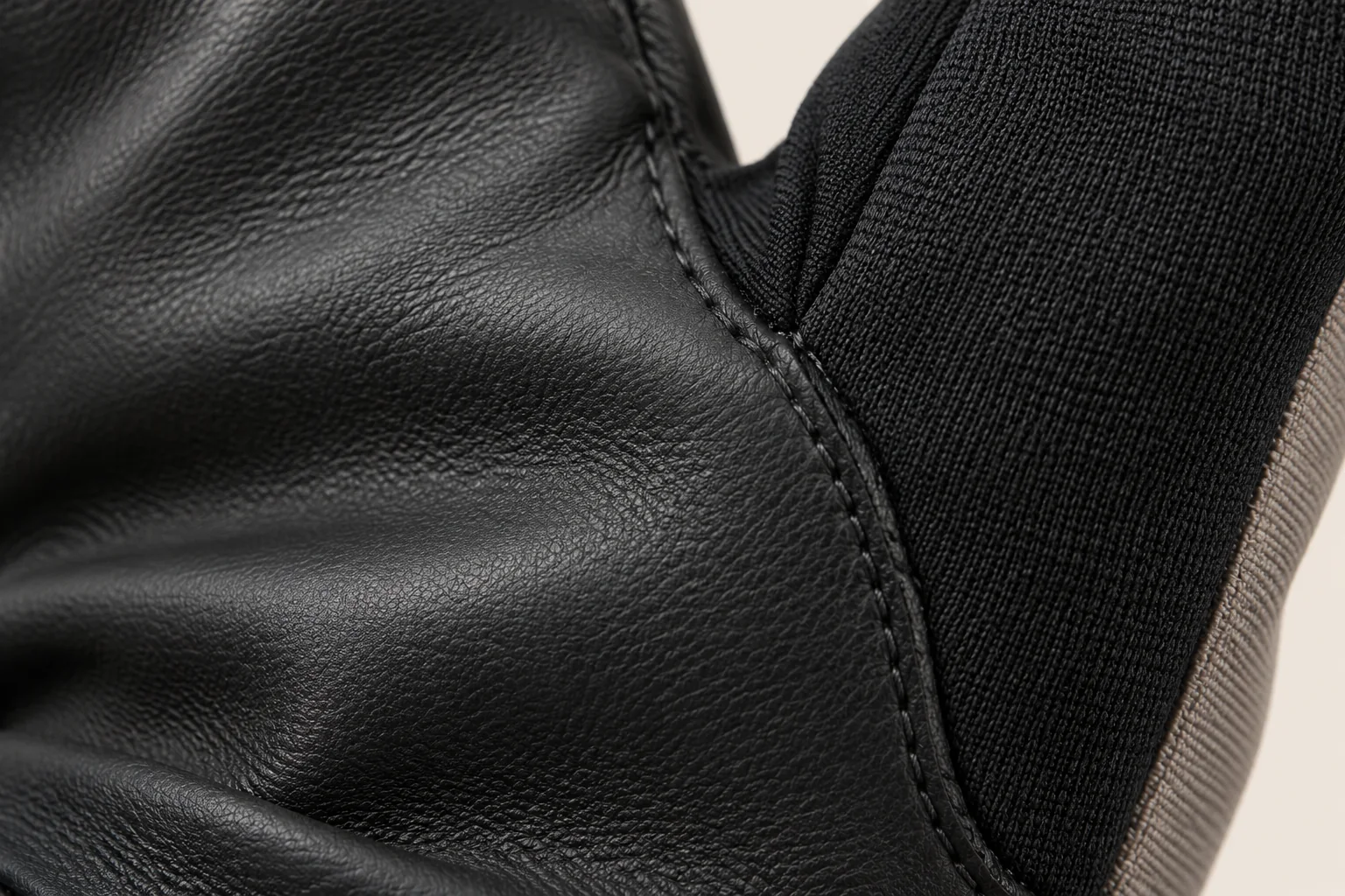 Mixed-panel touchscreen glove: macro black smooth palm to black side panel seam at thumb gusset.
