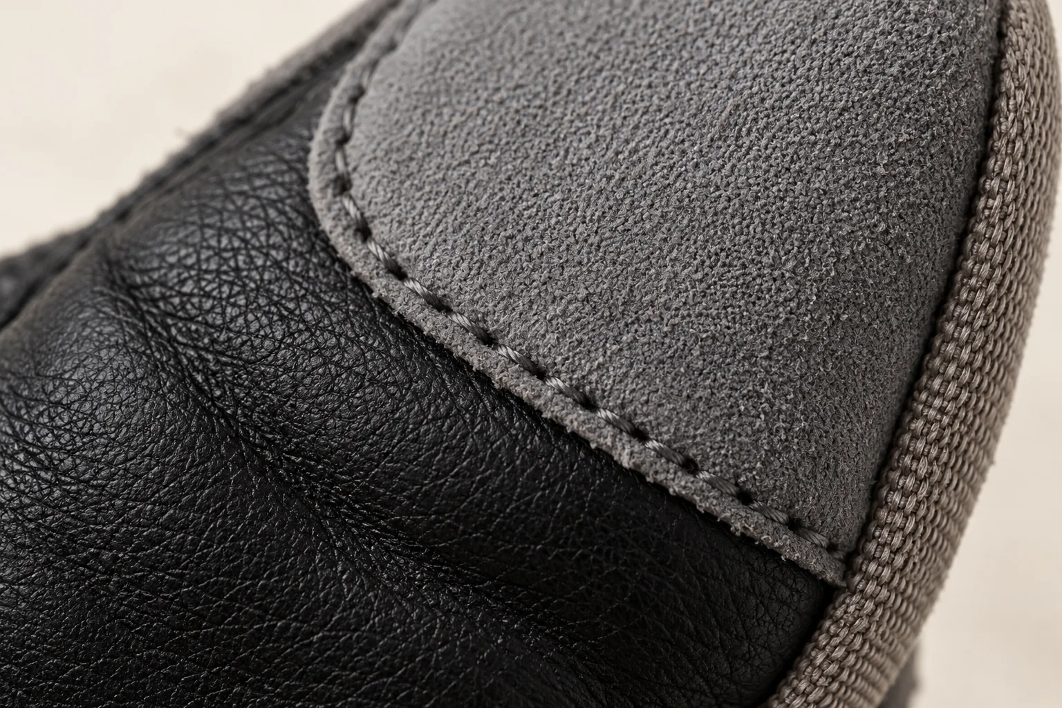 Mixed-panel touchscreen glove: extreme macro gray contact patch edge stitched onto black palm surface at index tip.