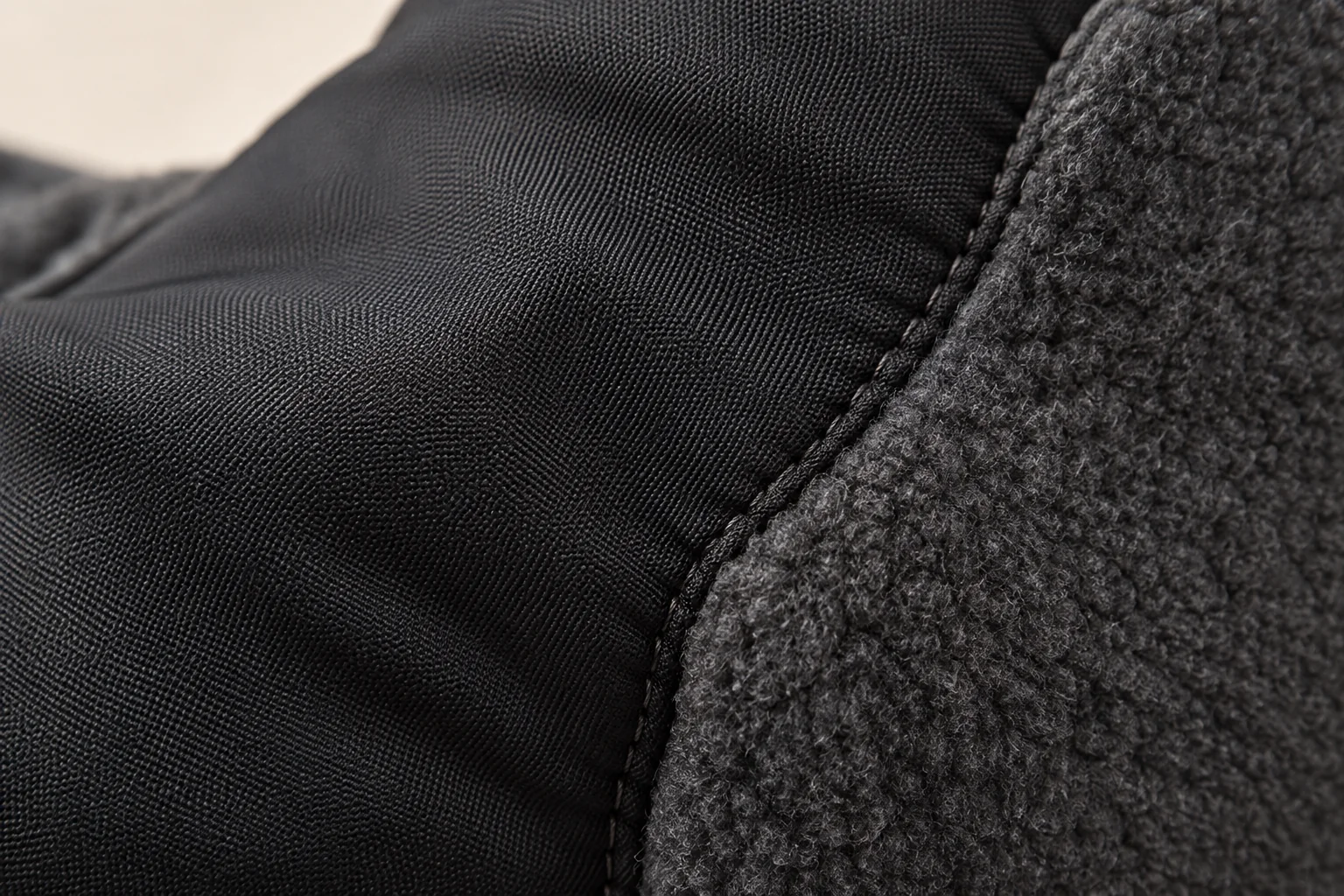 Panel-fleece glove: macro at black smooth woven thumb-side panel meeting charcoal fleece.