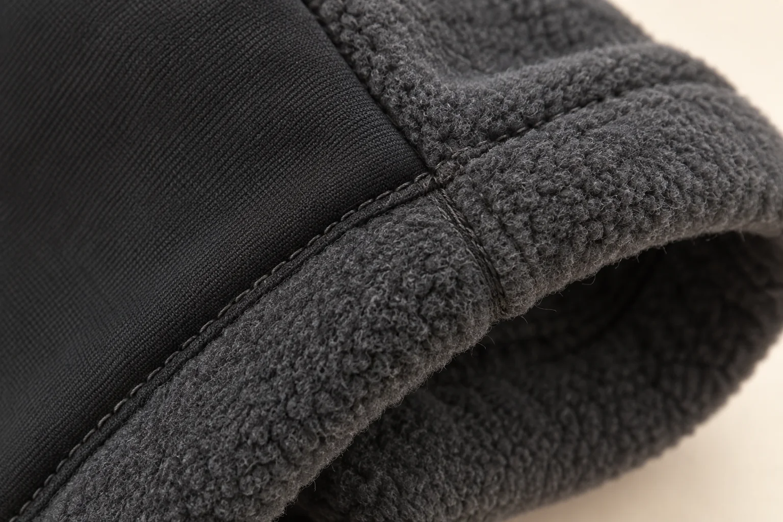 Charcoal panel-fleece glove: macro at cuff hem and its internal side-seam intersection.
