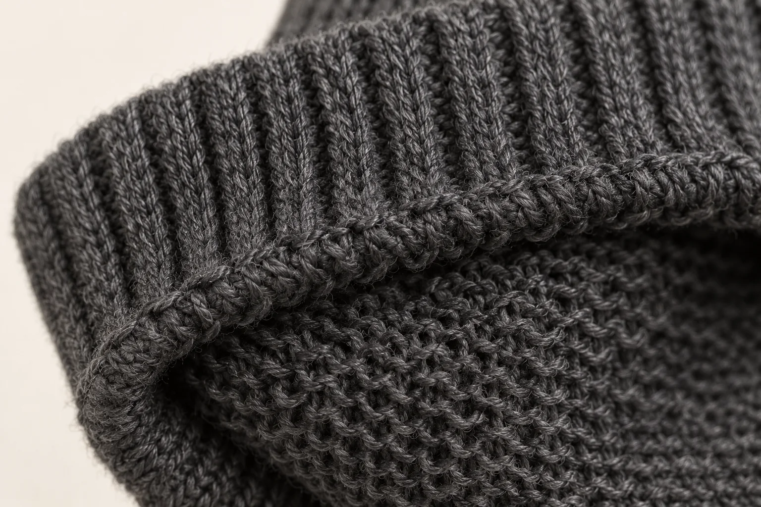 Charcoal knit glove: macro of the unlined inside just at the turned wrist edge, revealing reverse purl loops next to the vertical-rib hem.