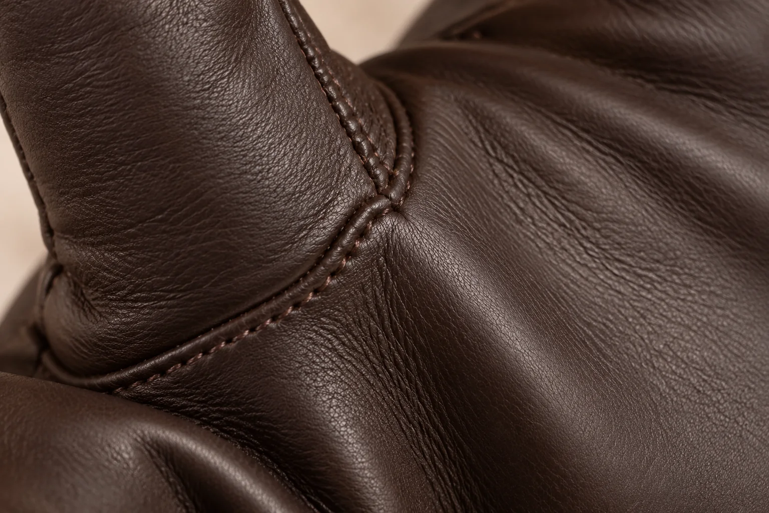Dark chocolate soft leather glove: macro at the gently curved palm-thumb seam.