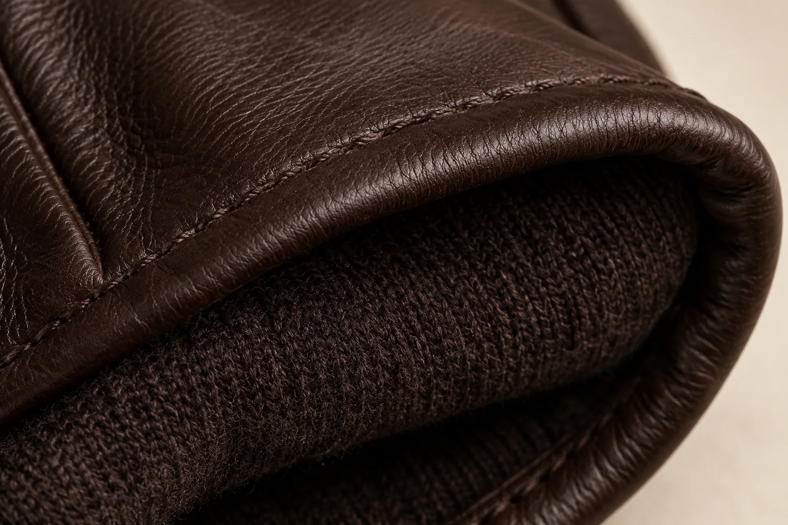 Dark chocolate glove: macro inside cuff showing dark fine-knit lining meeting a turned dark-brown leather edge.